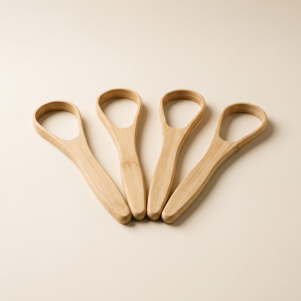 Four bamboo tongue scrapers arranged in a fanned row on an ivory background