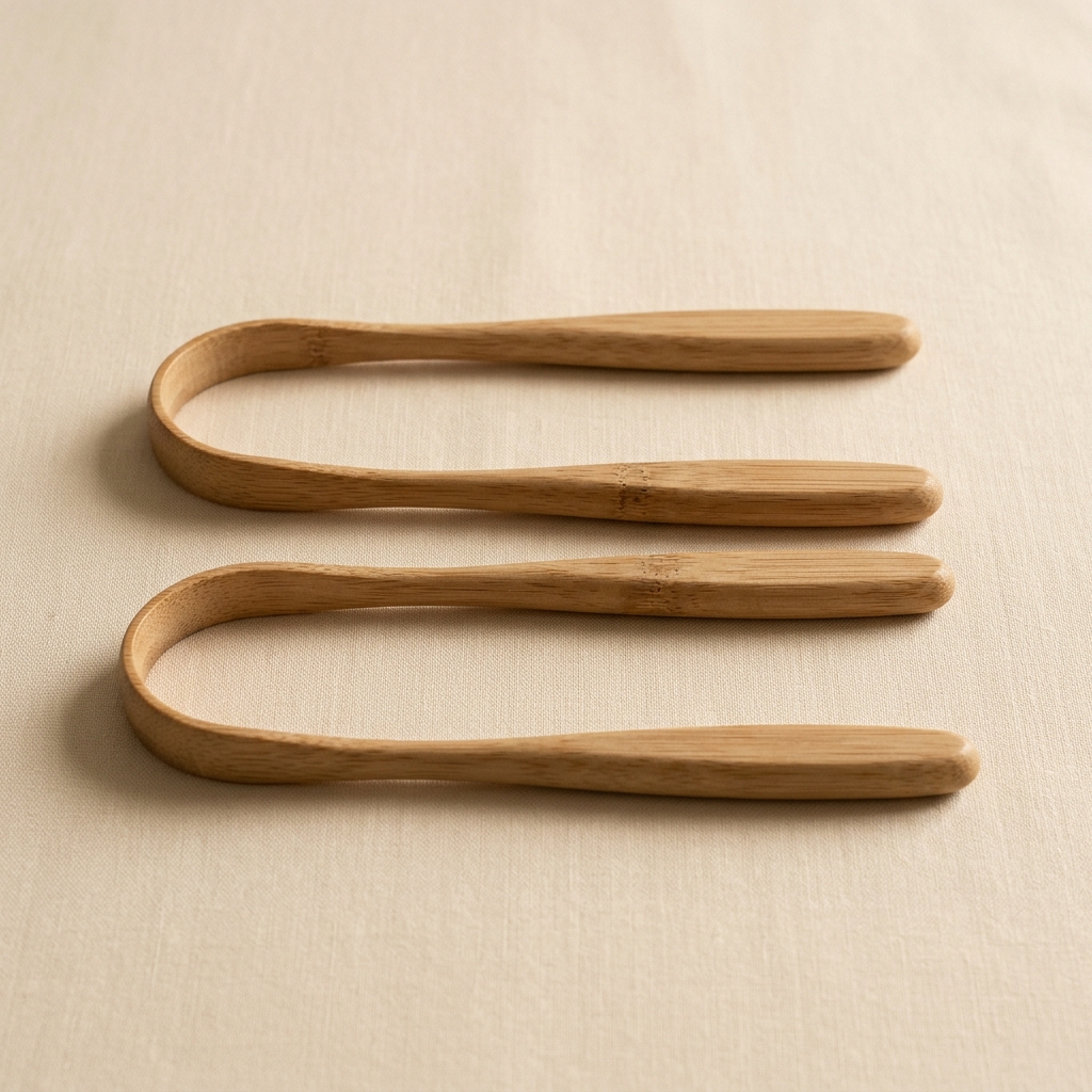 Two bamboo tongue scrapers laid parallel on a warm ivory background