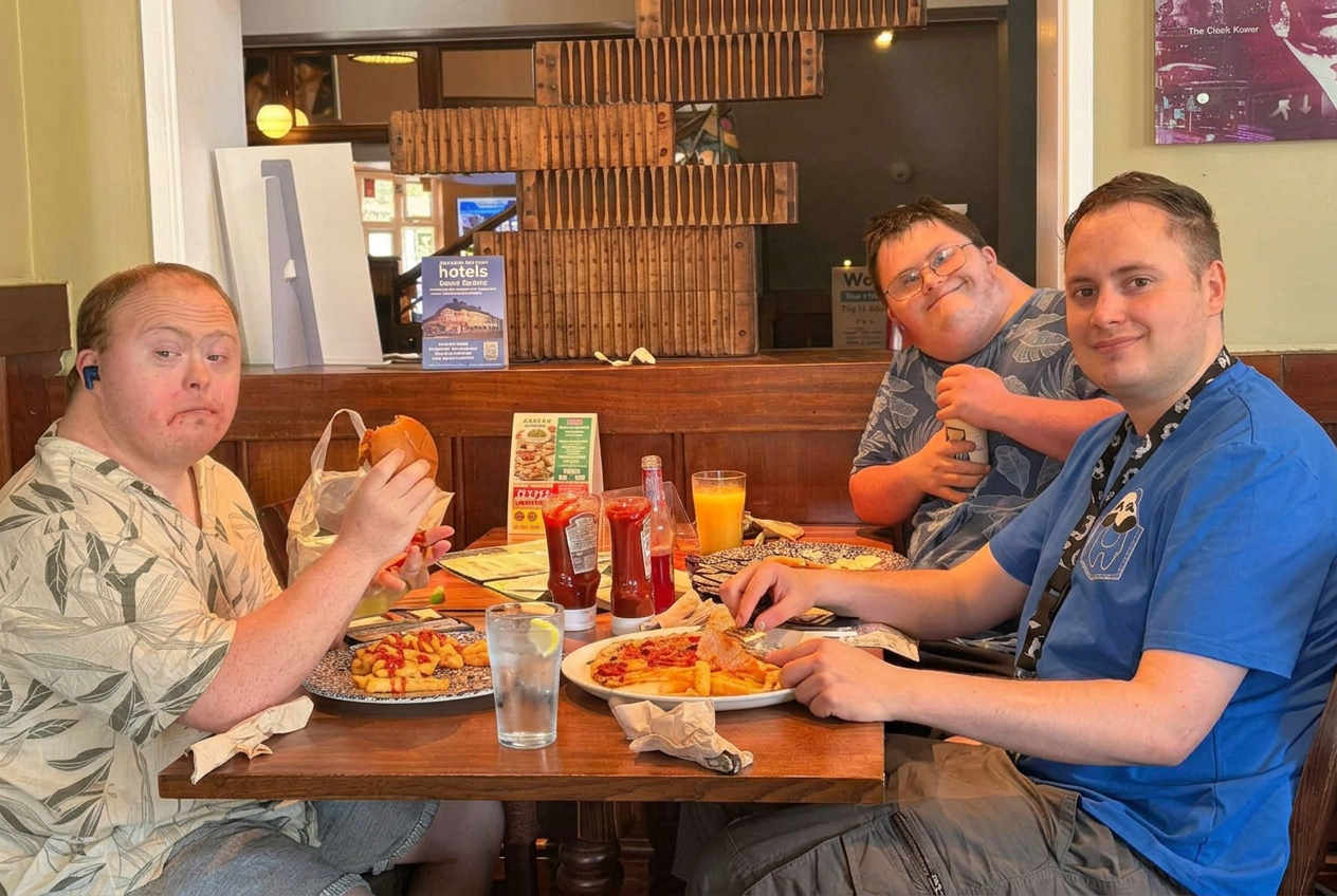 Three people we support enjoying a meal out together at a pub, practising ordering and eating in the community.